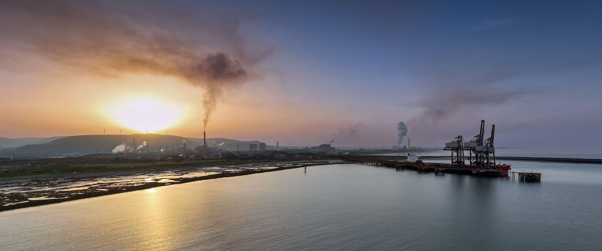 A sunset over a calm body of water with industrial structures and smokestacks in the background.