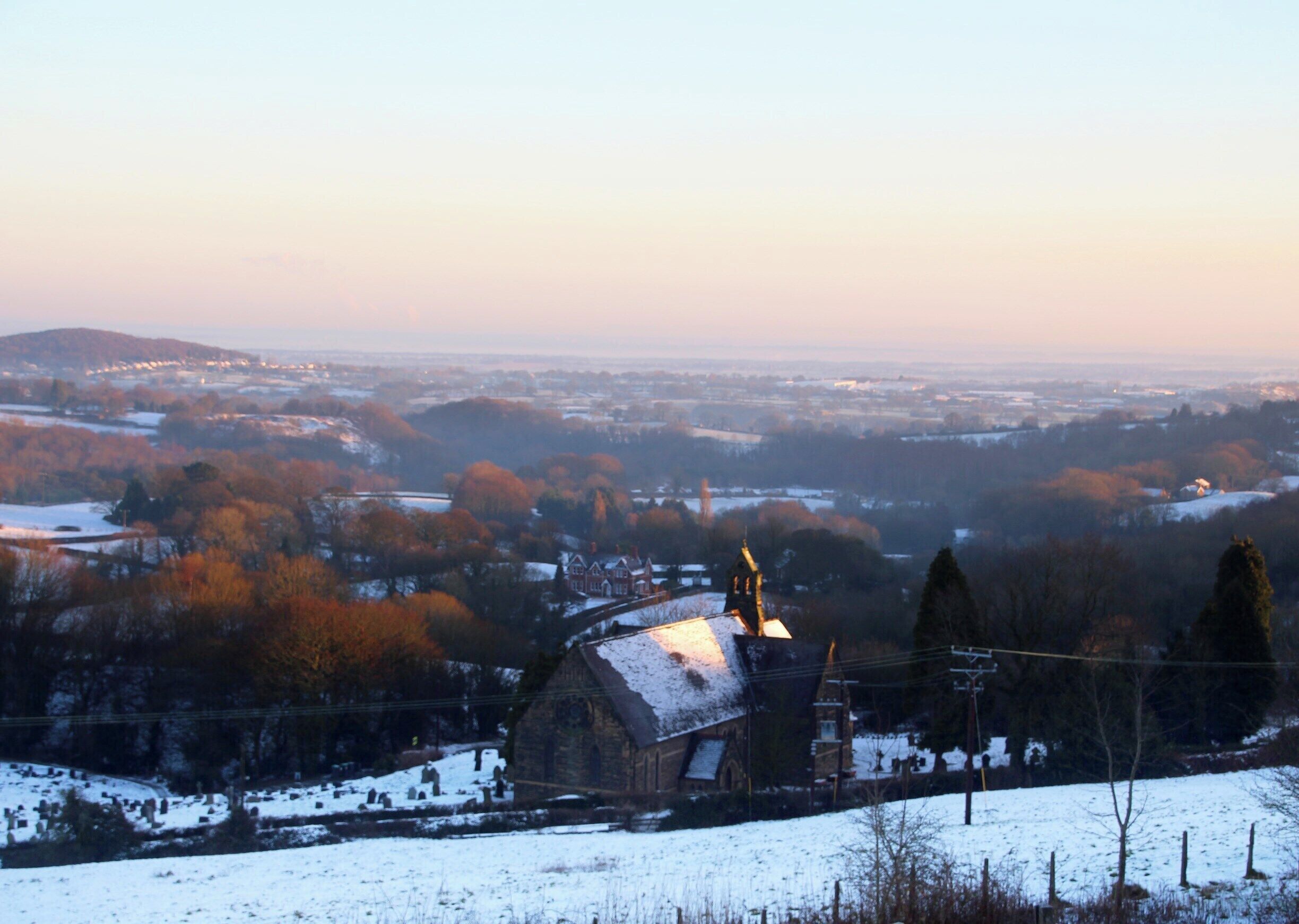 A snow-covered landscape with a church and distant hills.