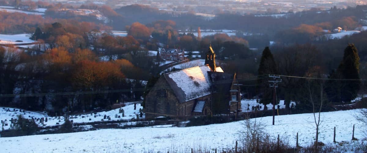 Schneebedeckte Landschaft mit einer Kirche und sanften Hügeln im Hintergrund.