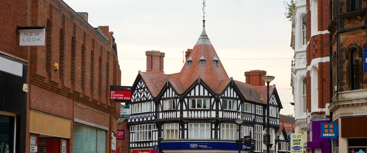 A traditional half-timbered building with a pointed roof, surrounded by modern shops and pedestrians.