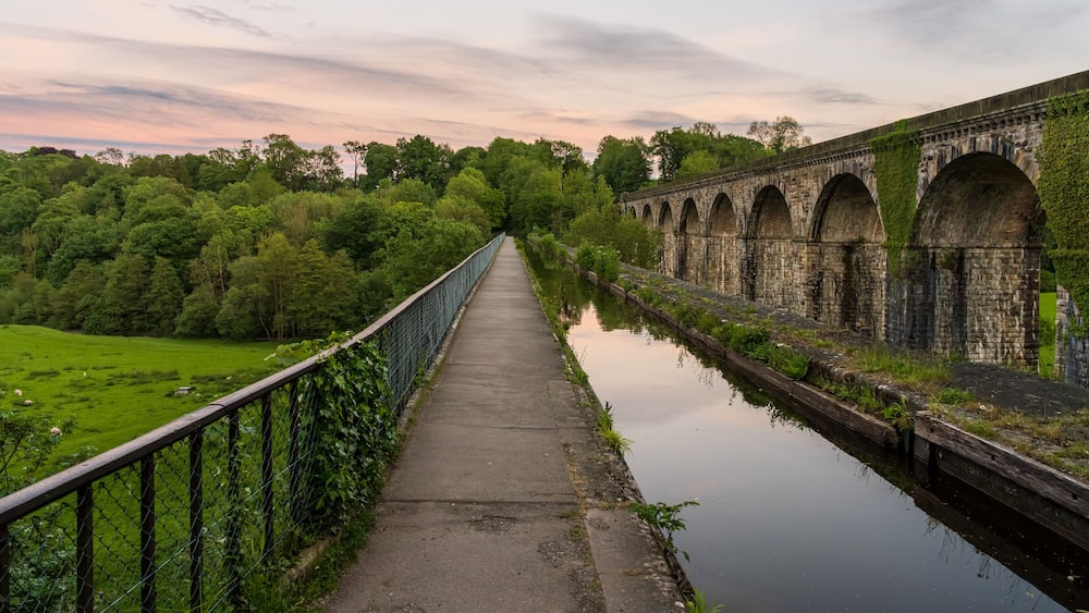 Un pont enjambant un canal, avec un chemin sur un côté et un champ herbeux de l’autre.