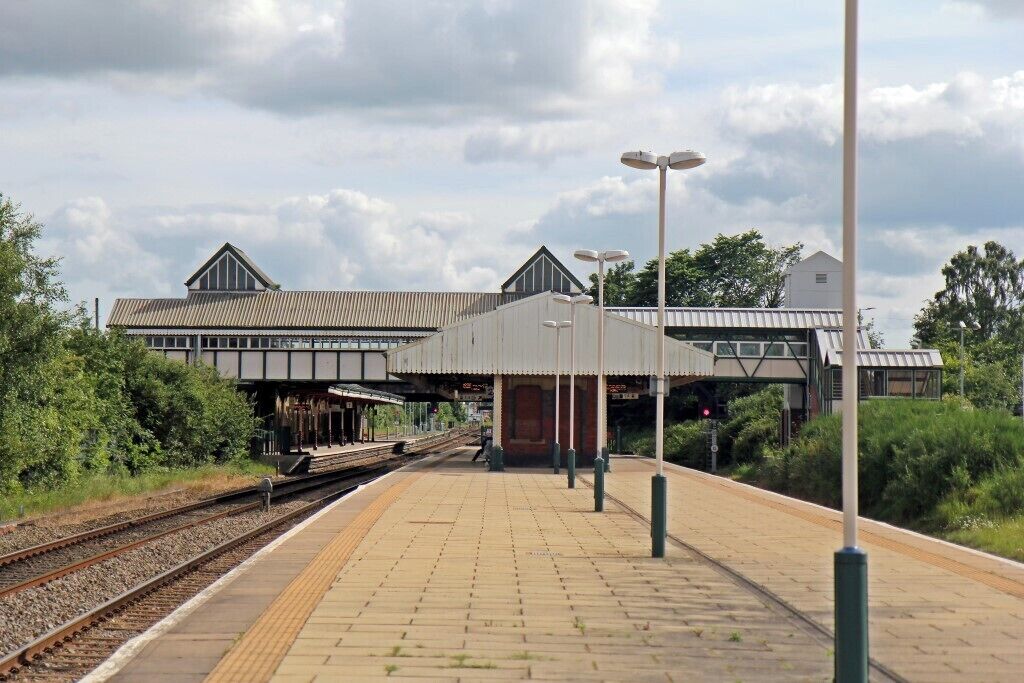 Ein Bahnhof mit überdachter Bahnsteig, Gleisen und einem Gebäude mit Blechdach.