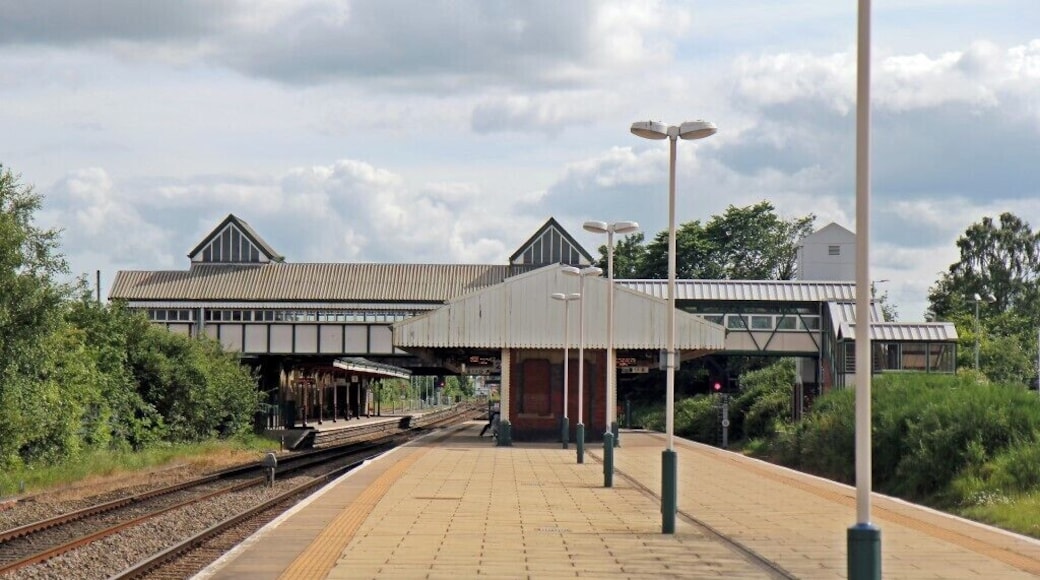 Ein Bahnhof mit überdachter Bahnsteig, Gleisen und einem Gebäude mit Blechdach.