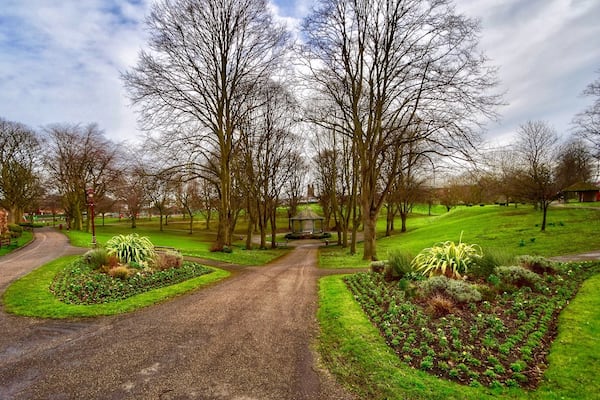 Un parc avec un sentier dallé, des arbres sans feuilles et un kiosque.