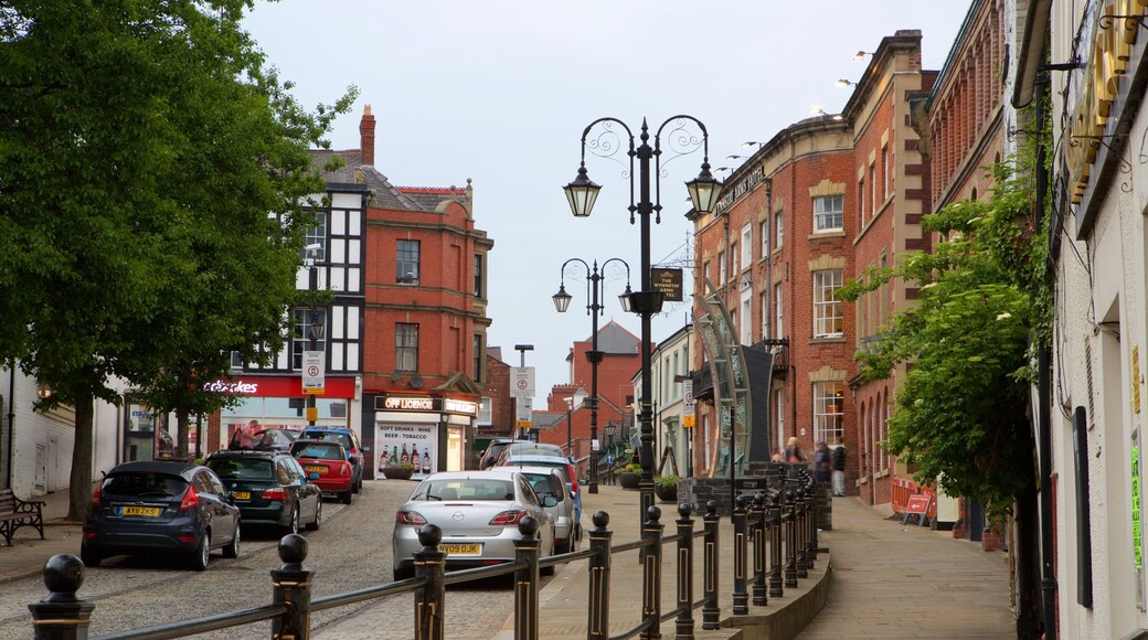 A cobblestone street lined with historic buildings, parked cars, and street lamps.