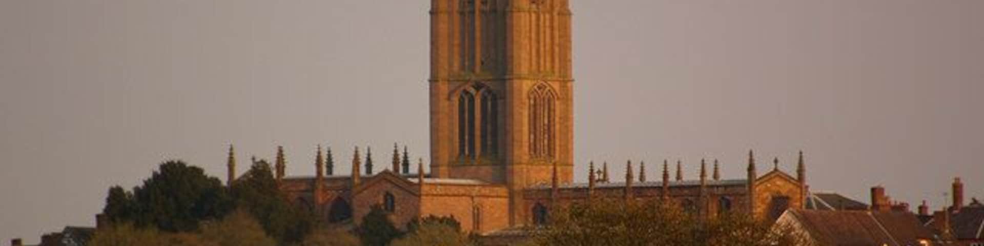 Una alta torre de iglesia de arquitectura gótica, rodeada de edificios residenciales y árboles.