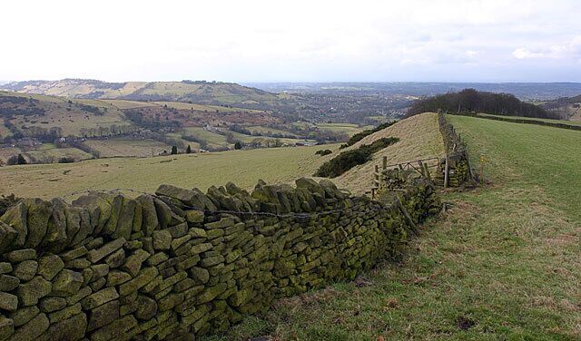 A stone wall, grassy fields, and rolling hills in the distance.