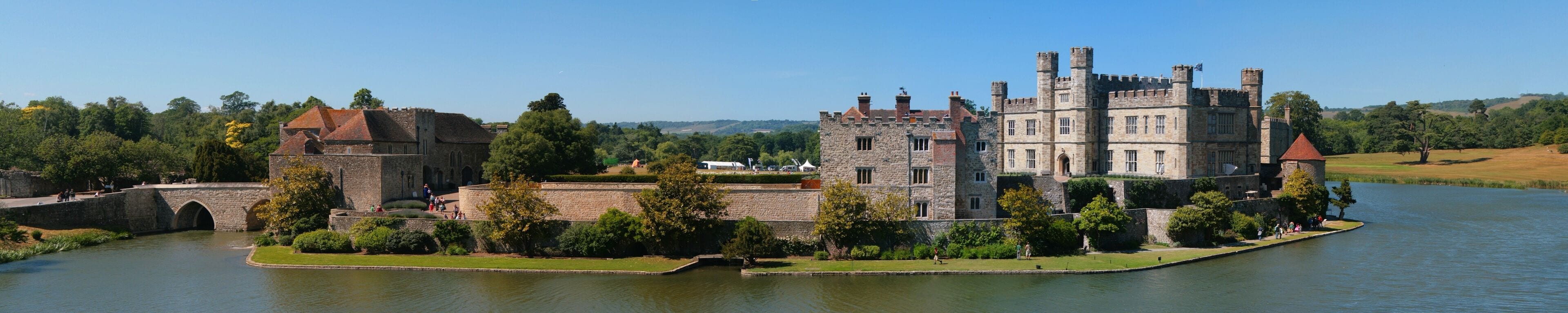 A historic castle by a river with a moat and a bridge.