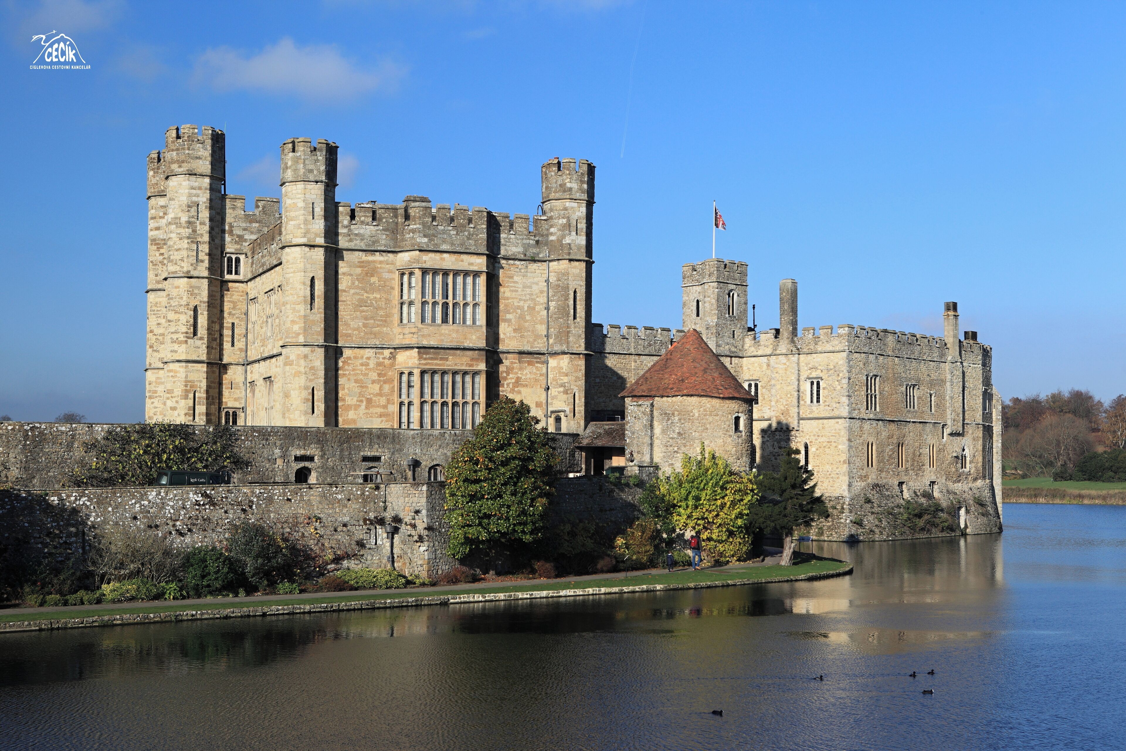 A historic castle with a moat, towers, and a flag.