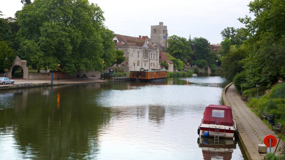 A river with a boat docked on the right, a stone bridge on the left, and a historic building in the background.