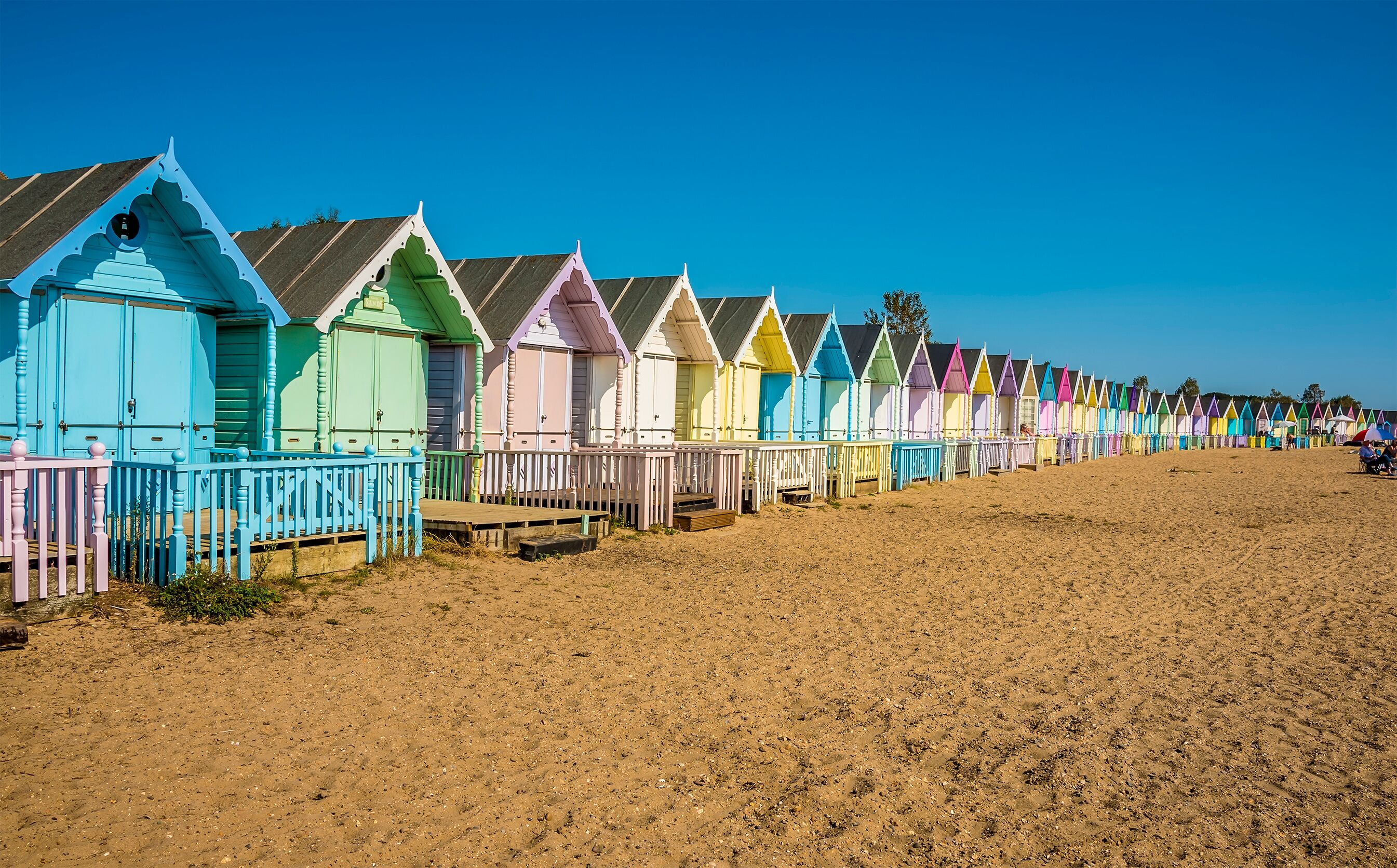 A wide-angle view along brightly coloured beach huts on West Mersea beach, UK in the summertime