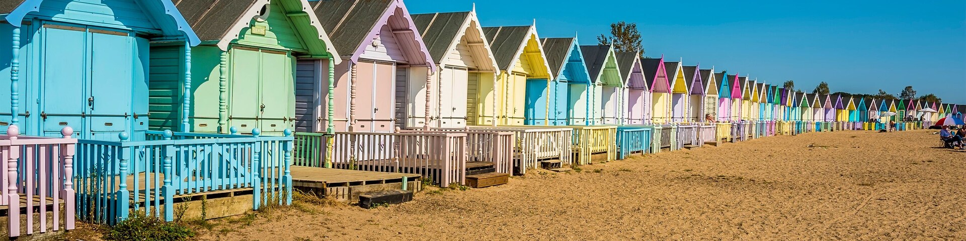 Fileira de cabanas coloridas à beira de uma praia arenosa.