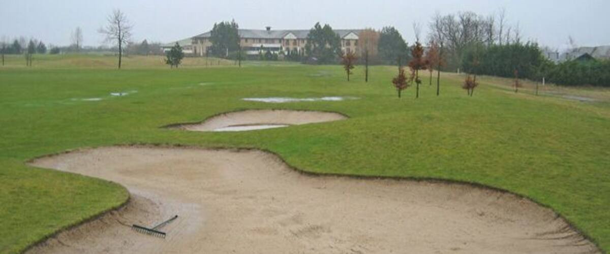 A golf course with sand bunkers and a building in the background.