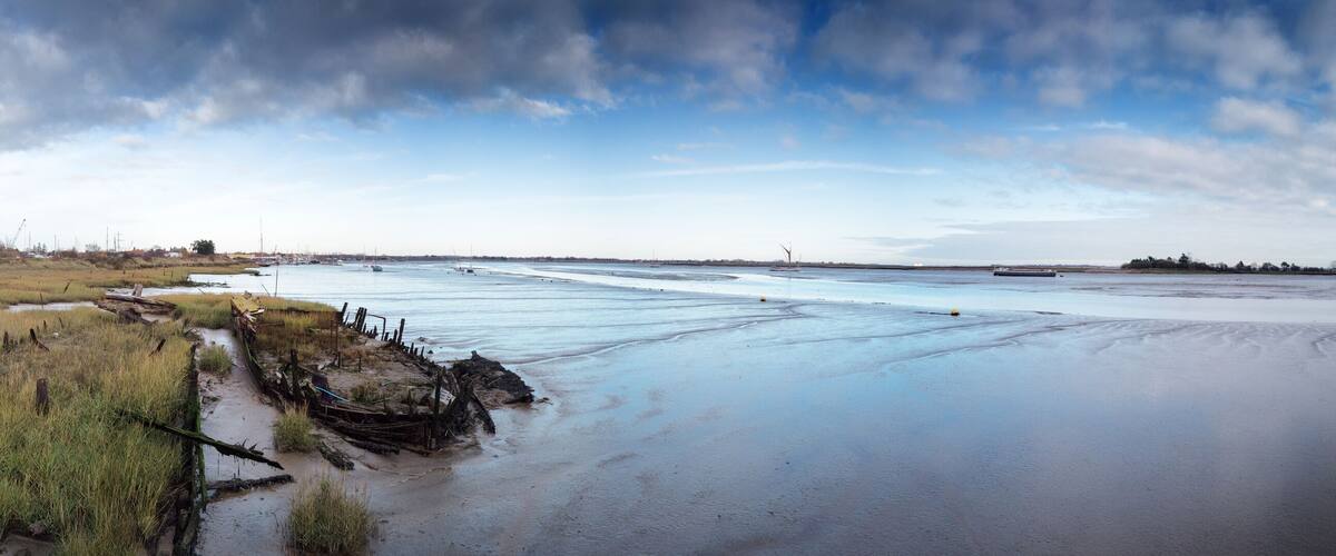 A coastal landscape with a sandy beach, grassy dunes, and a calm sea with boats.