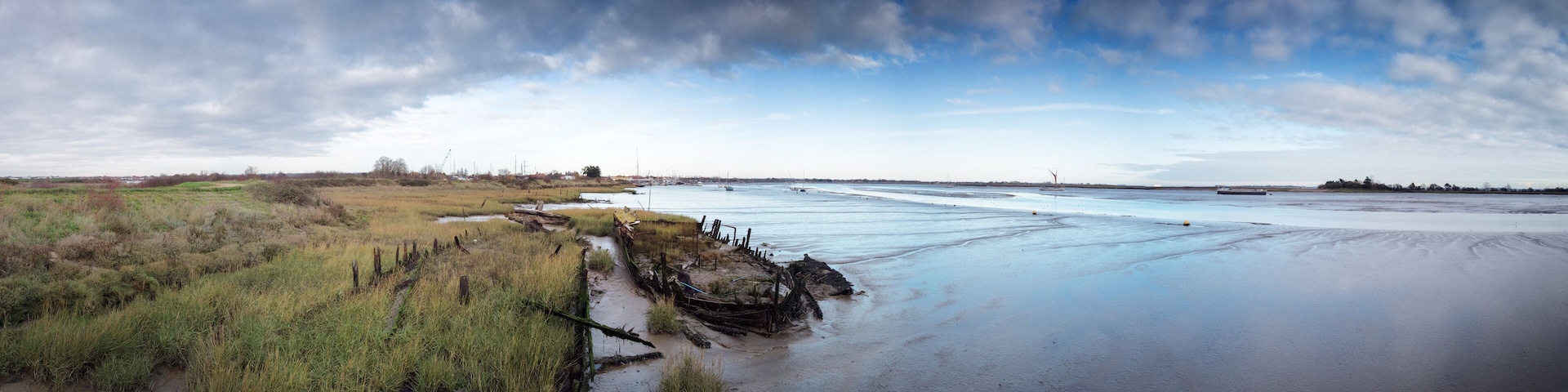 A coastal landscape with a sandy beach, grassy dunes, and a calm sea with boats.