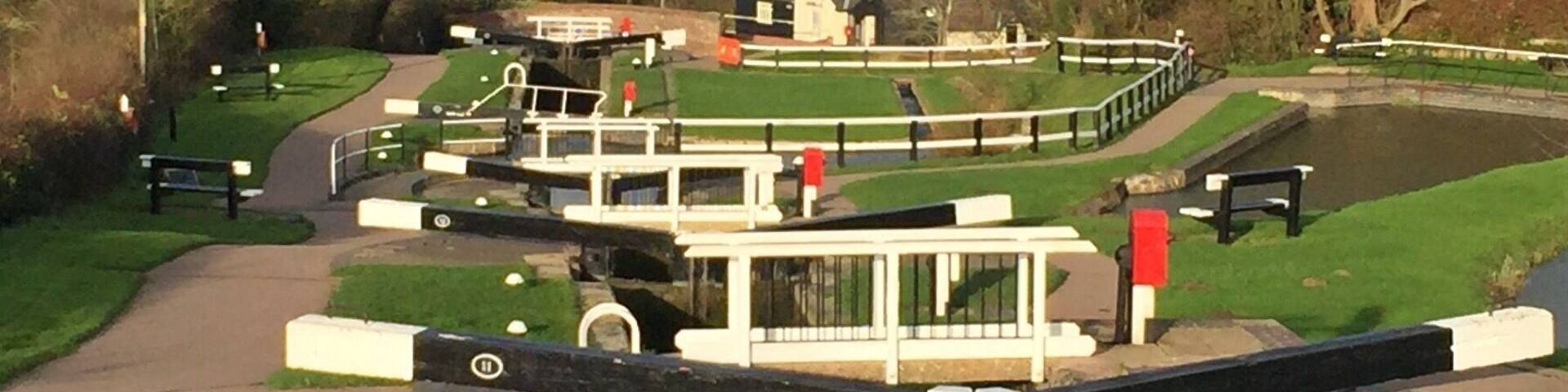 Un parque a orillas de un canal, con barcas, bancos y un pequeño edificio.