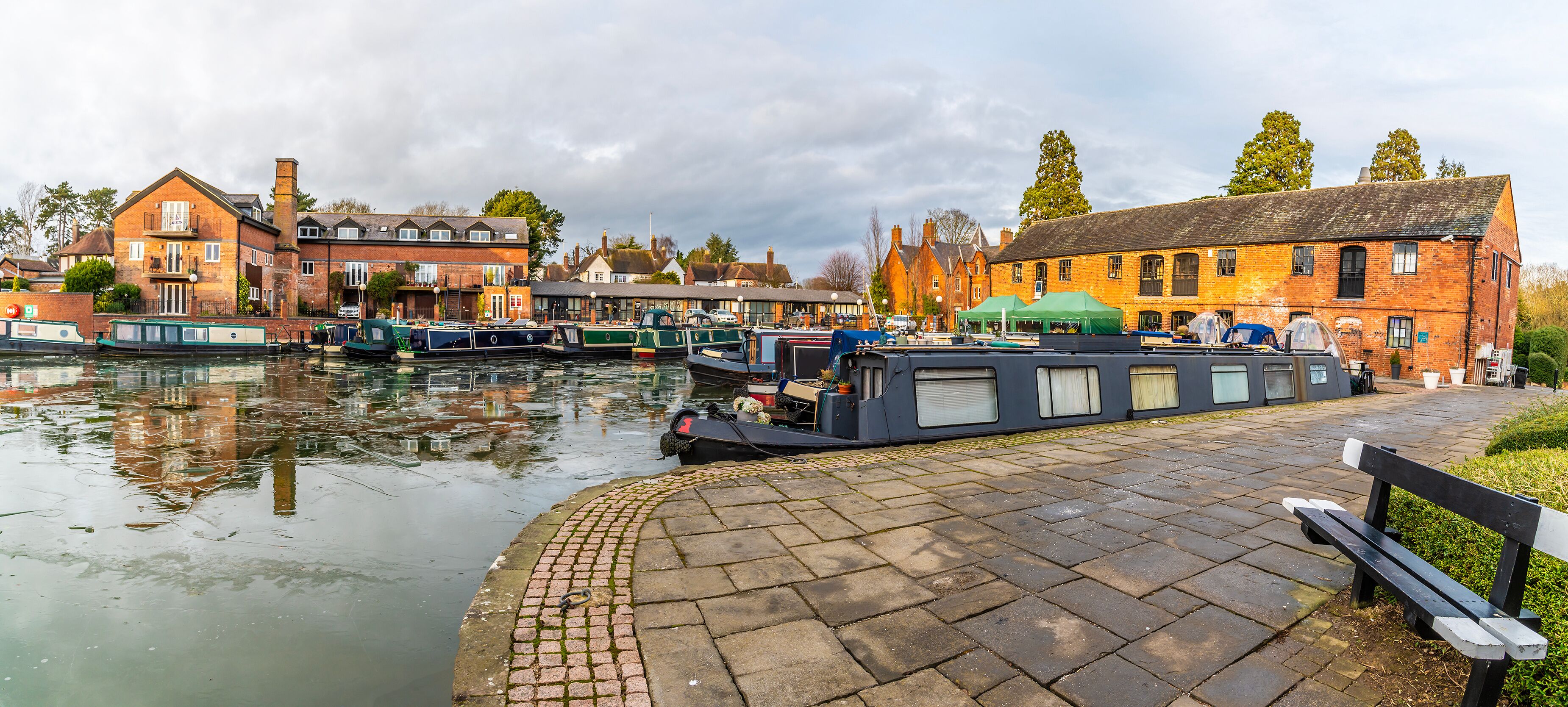 A canal with boats, brick buildings, and a bench.