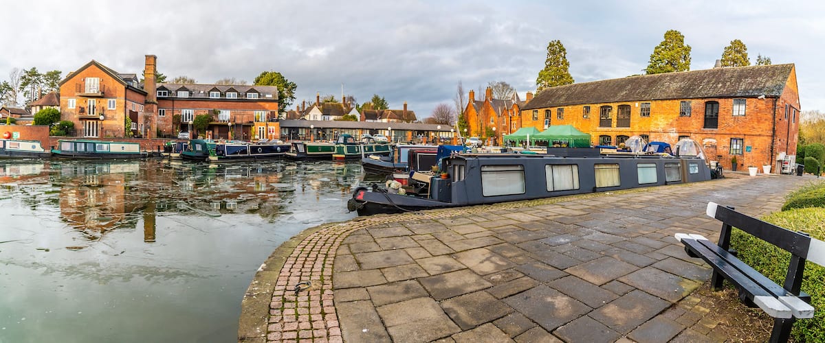 A canal with boats, brick buildings, and a bench.