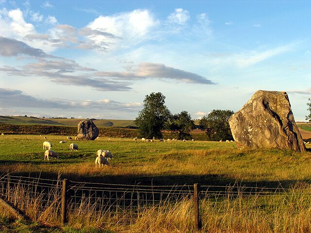 A rural landscape with sheep grazing, large boulders, and a fence.