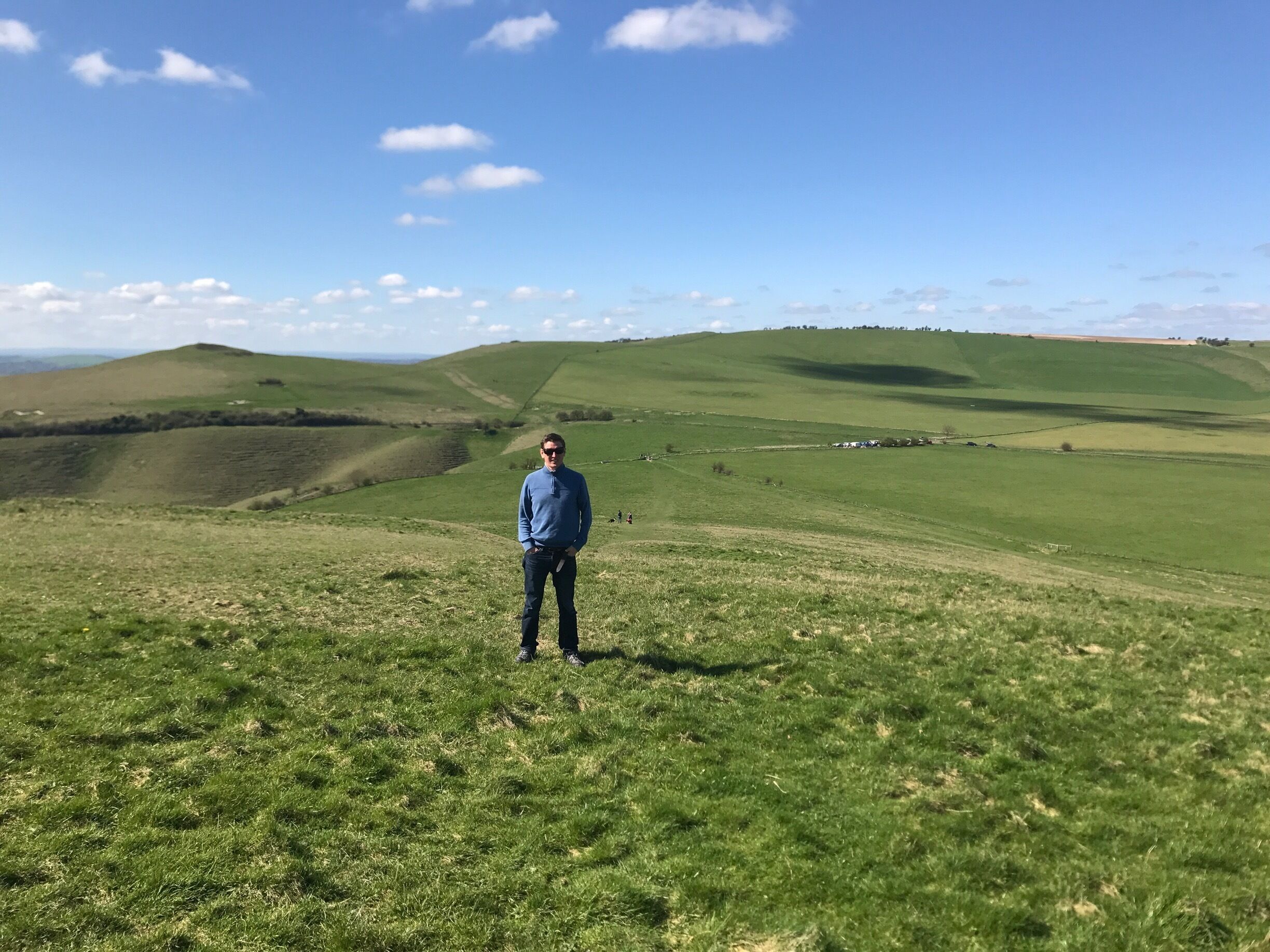 A person standing on a grassy hill with rolling hills in the background.