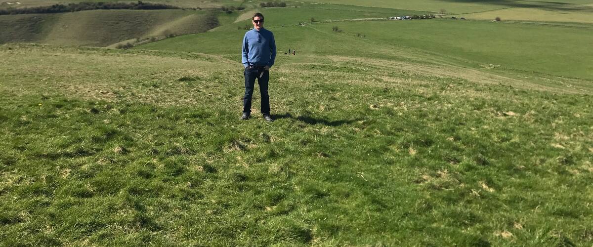A person standing on a grassy hill with rolling hills in the background.