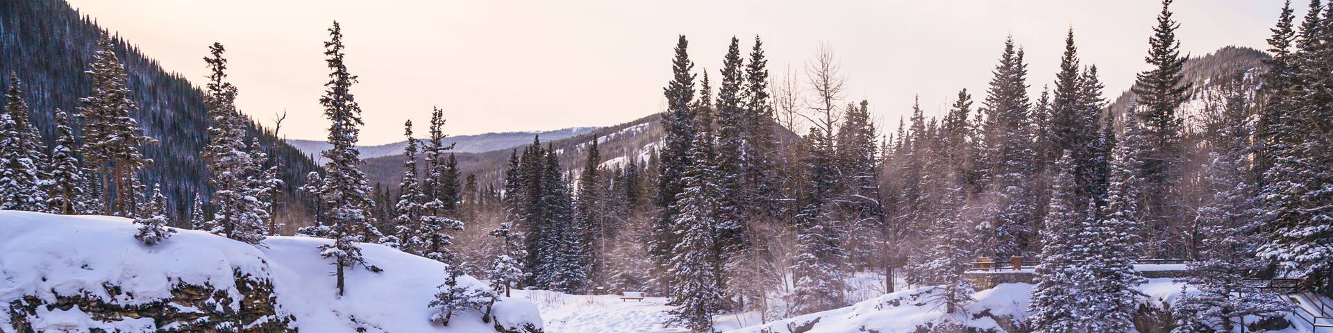 A snow-covered waterfall in a forested valley with rocky cliffs.