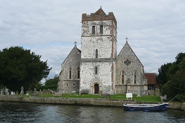A historic stone church with a tower and arched windows by a calm river.