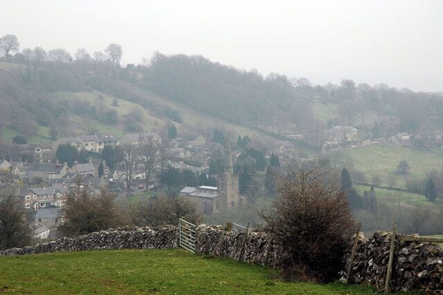 A foggy rural landscape with stone walls, a stone gate, and a distant village with a church tower.