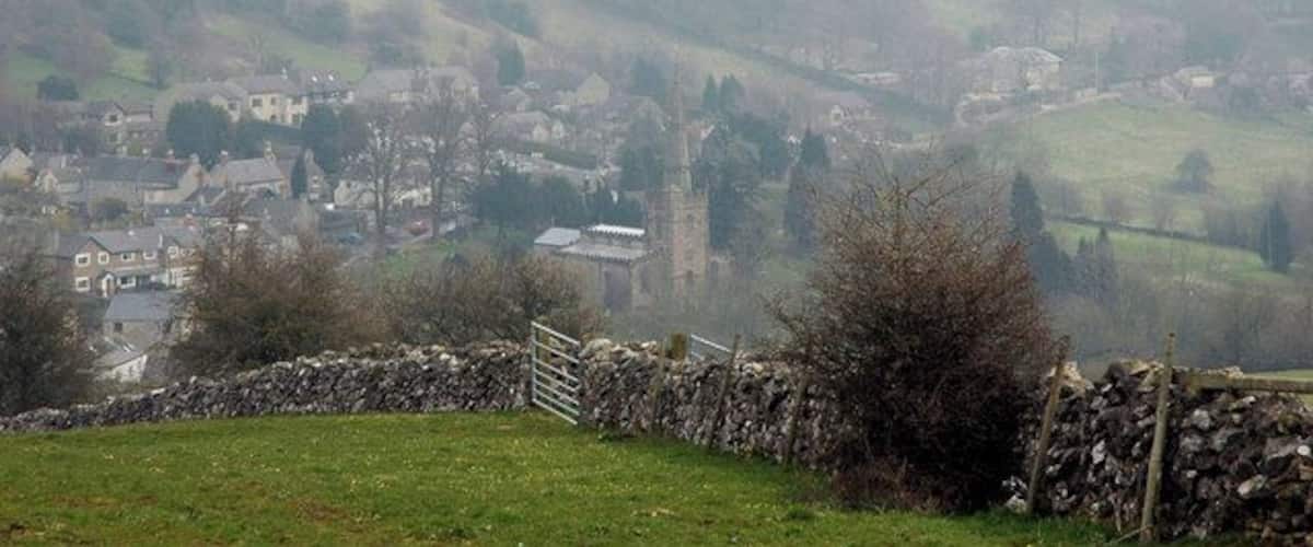 A foggy rural landscape with stone walls, a stone gate, and a distant village with a church tower.