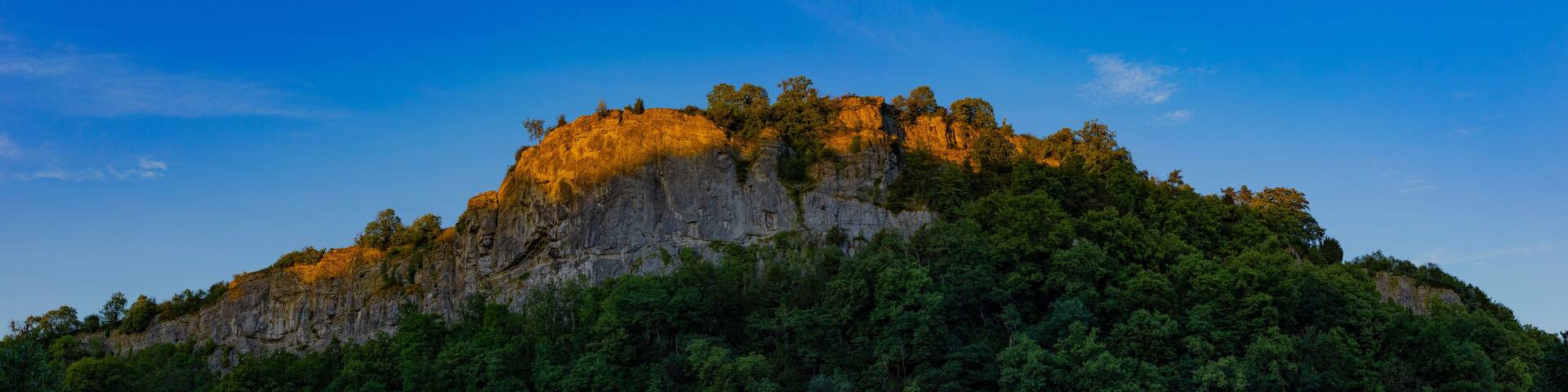 Sunlight illuminating top of rocky outcrop against blue sky; Matlock, Derbyshire, England