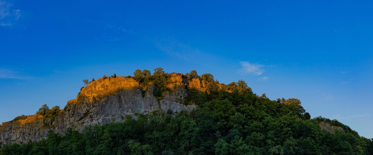 A mountain with a forested peak and a clear blue sky.