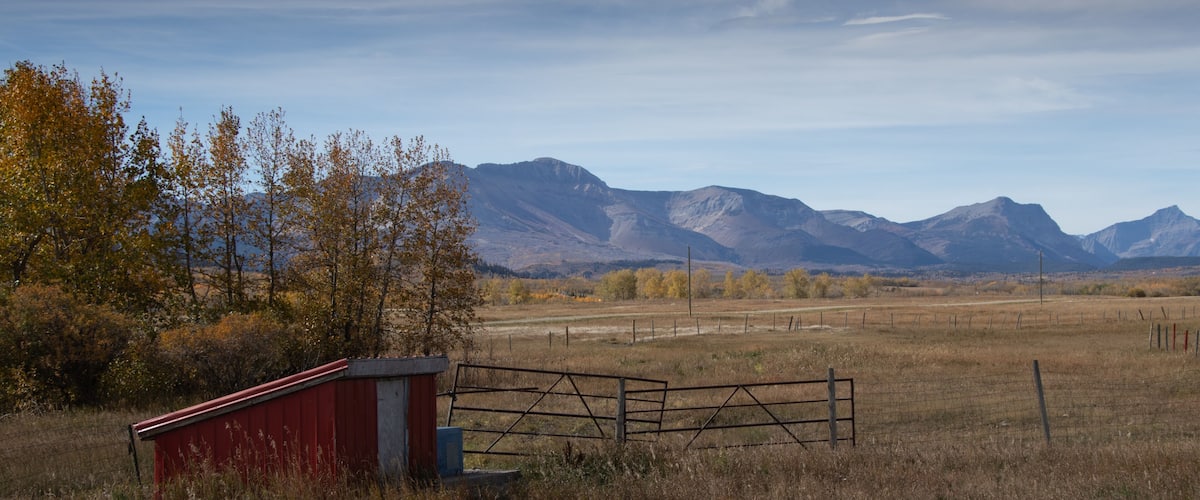 A rural landscape with a red barn, a metal gate, and mountains in the background.