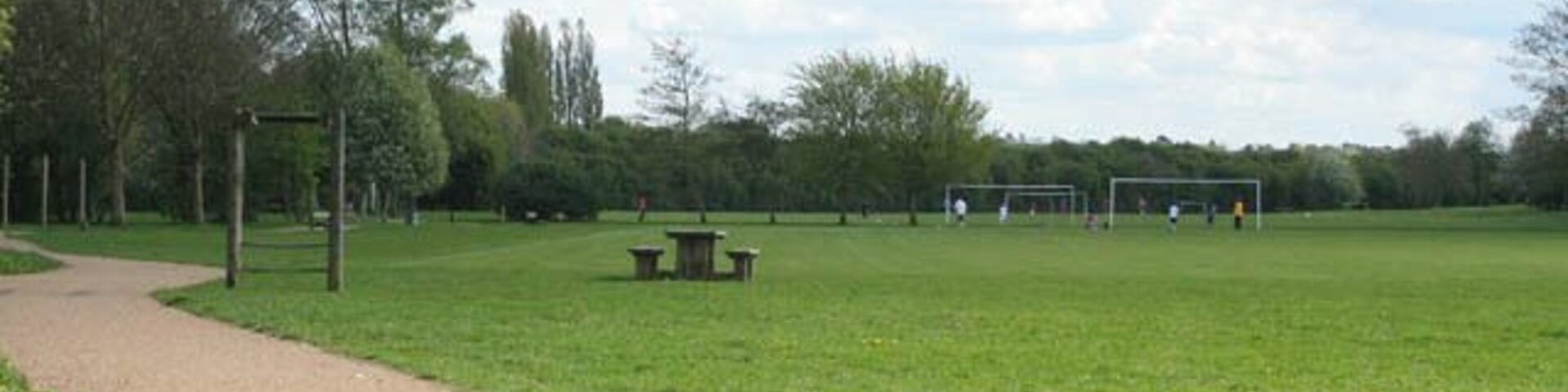 Un parque con un camino de grava, una mesa de picnic y porterías de fútbol.