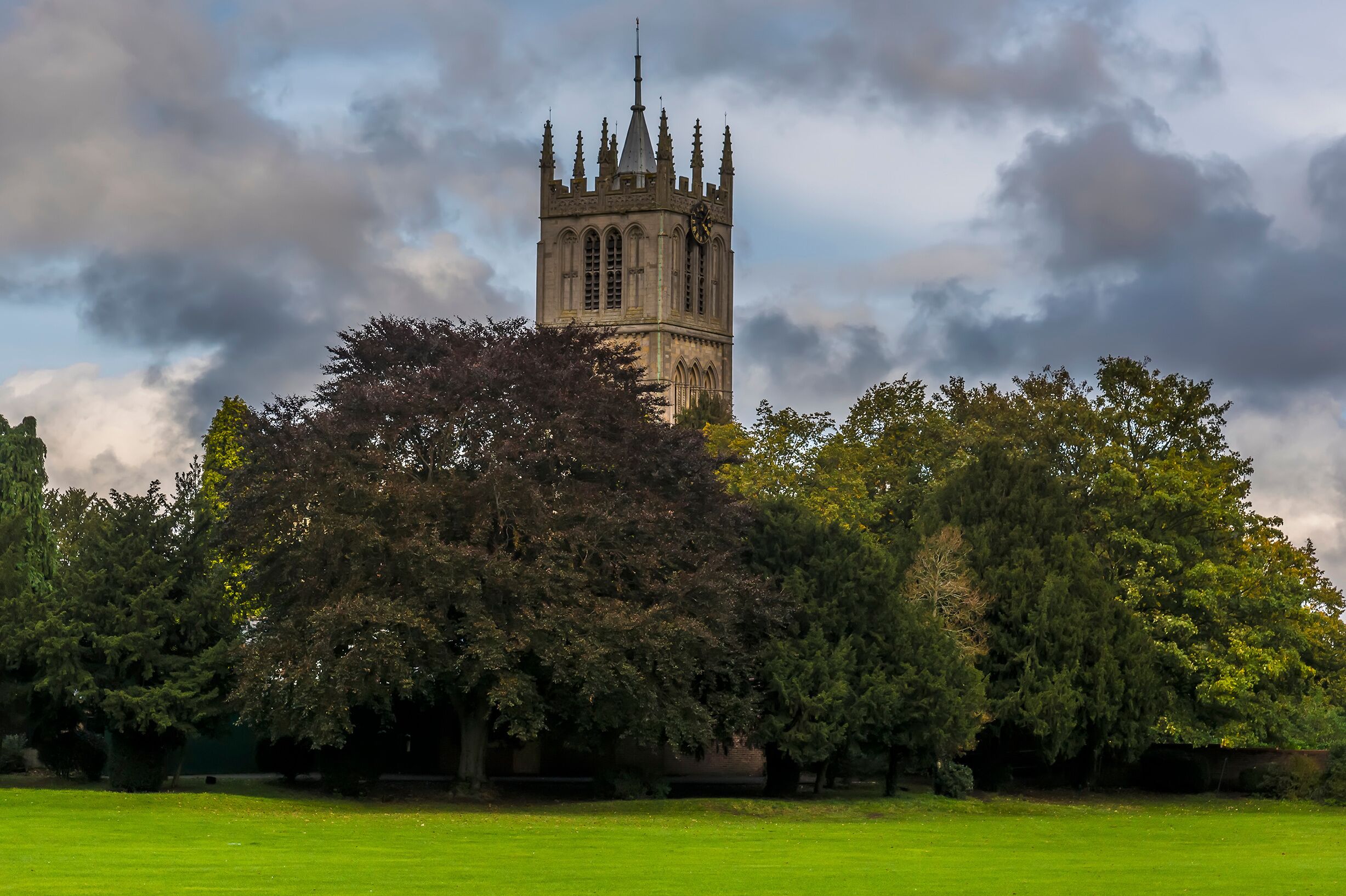 A historic tower with a clock, surrounded by lush green trees and a well-maintained lawn.