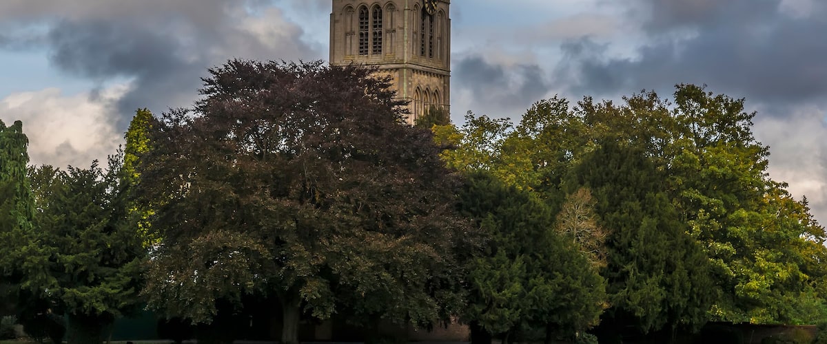 A historic tower with a clock, surrounded by lush green trees and a well-maintained lawn.