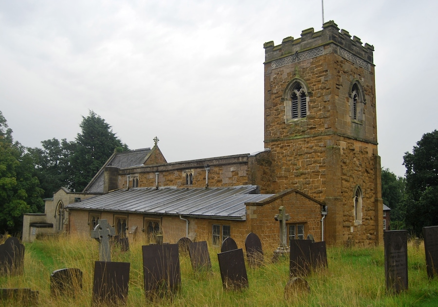 A church with a tall tower and multiple tombstones in the foreground.