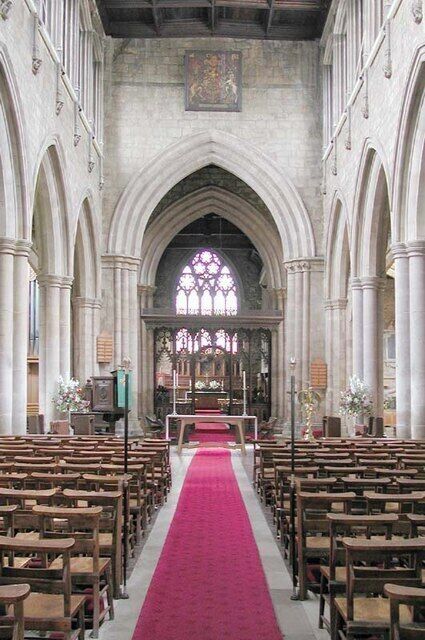 Interior de una iglesia con pasillo de moqueta roja, bancos de madera y un gran ventanal con vitrales.