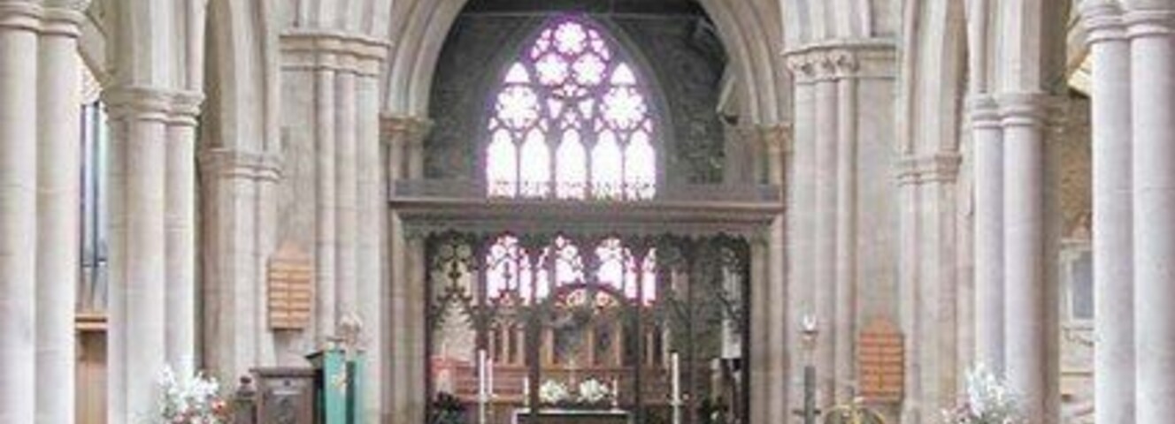 Interior de una iglesia con pasillo de moqueta roja, bancos de madera y un gran ventanal con vitrales.