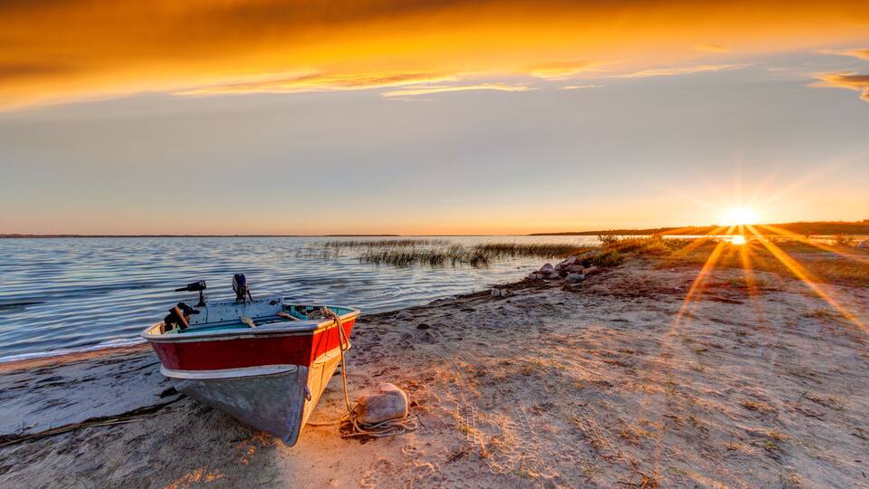 A boat on a sandy beach with the sun setting in the background.
