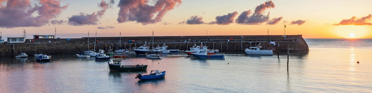 Ein Hafen bei Sonnenuntergang mit vertäuten Booten und einer anlegenden Pier.