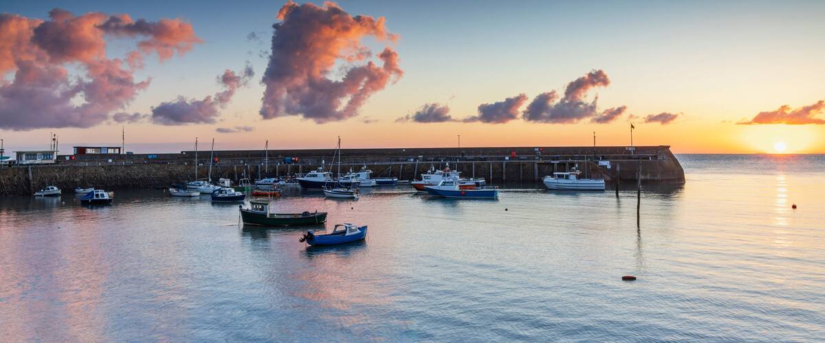 Ein Hafen bei Sonnenuntergang mit vertäuten Booten und einer anlegenden Pier.