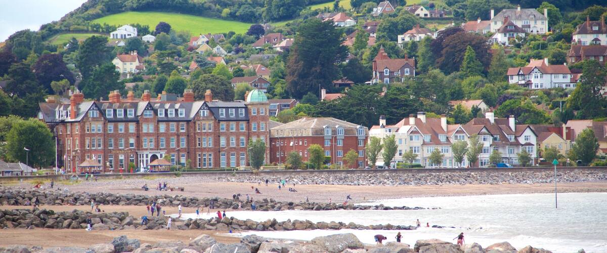 A coastal town with historic buildings, a rocky beach, and a hill with houses.