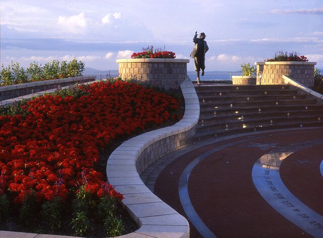 A person jumping on a curved staircase with red flowers and a view of the ocean.