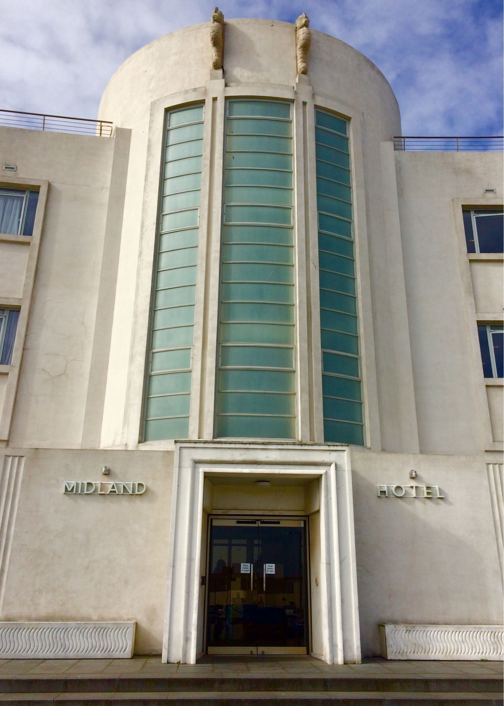 A building with a curved facade, large windows with green shutters, and signs reading "MIDLAND HOTEL".