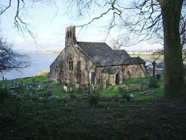 A stone church with a graveyard and a body of water in the background.