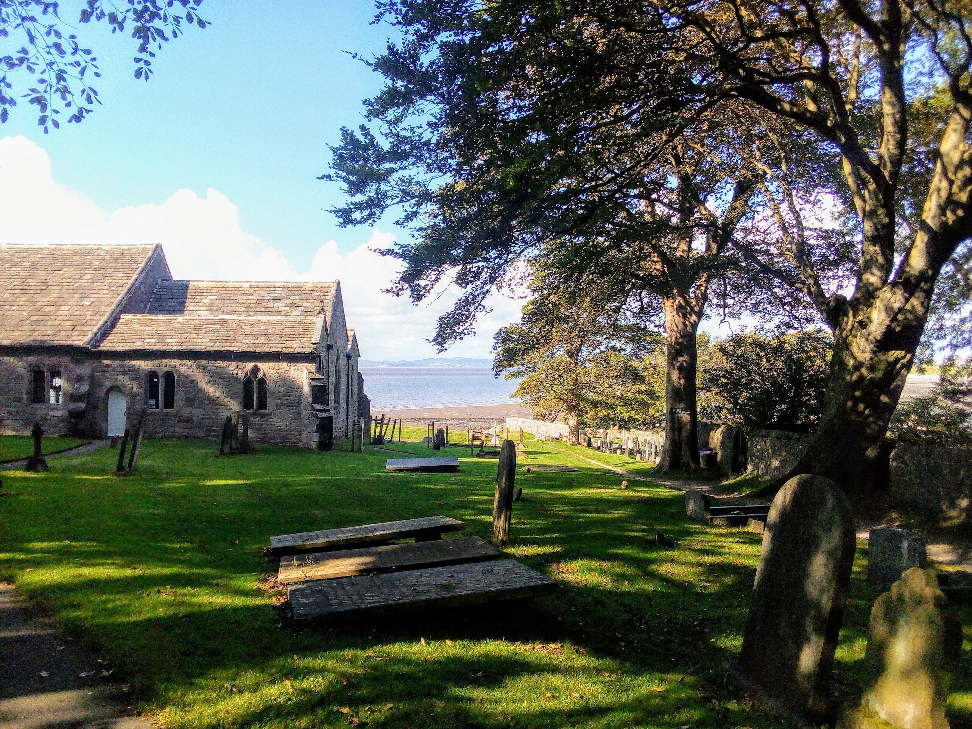 Una iglesia de fachada de piedra y un cementerio cubierto de césped con lápidas.