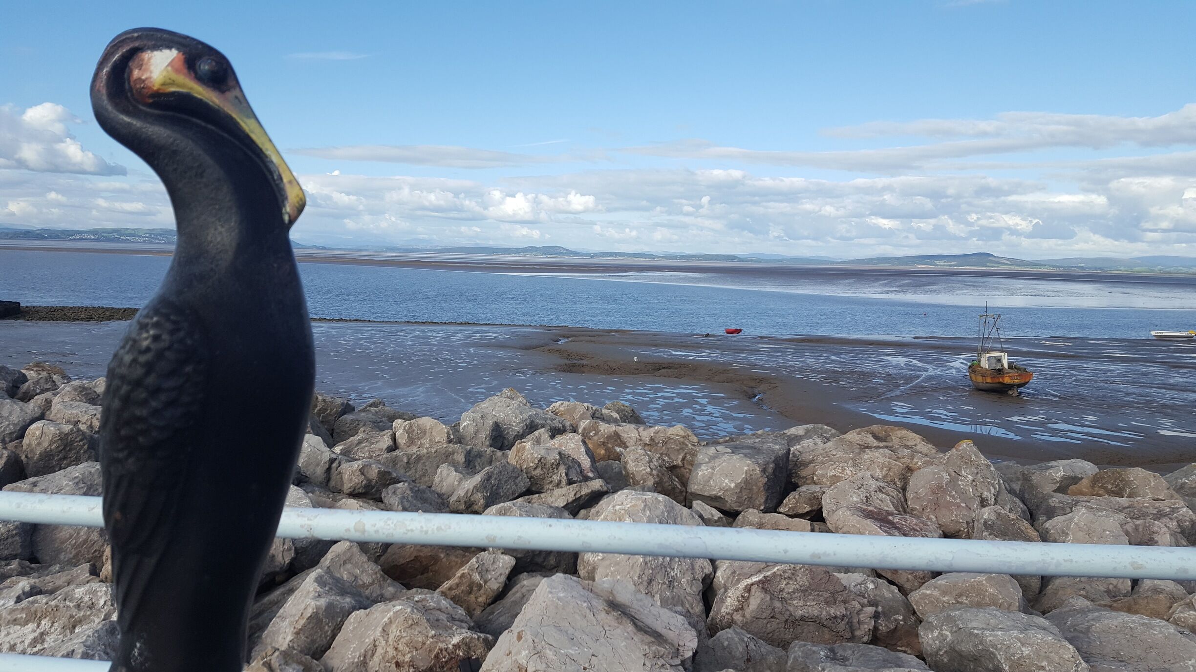 A rocky shoreline with a bird, a calm sea, and distant mountains.
