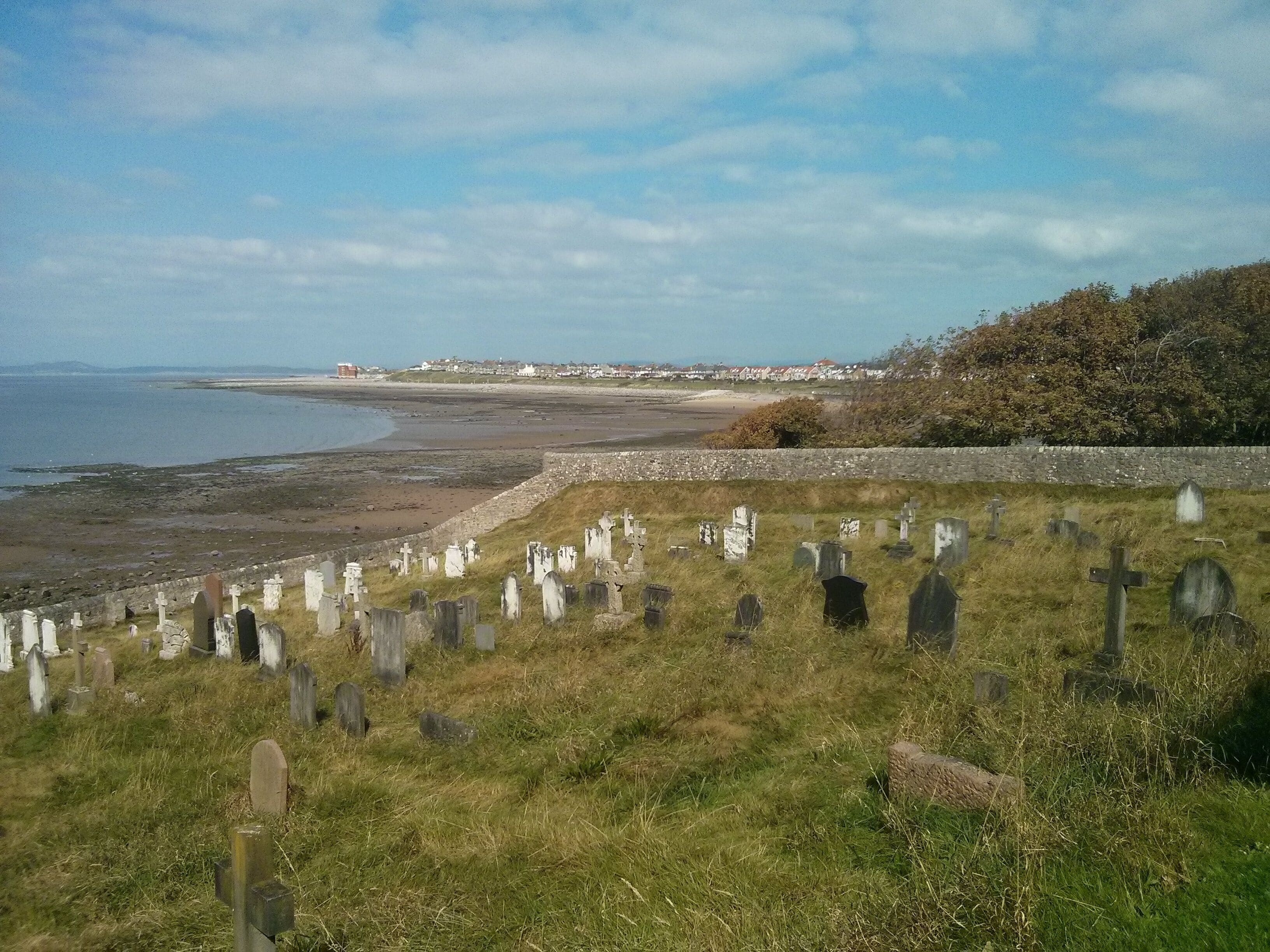 A coastal cemetery with headstones and a beach in the background.