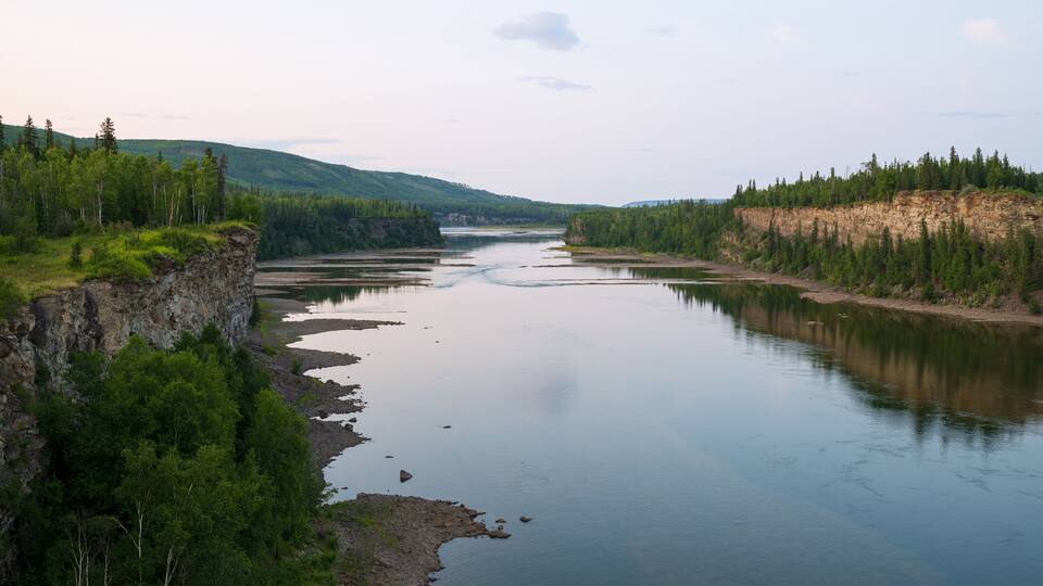 A river winding through a forested valley with steep cliffs on one side and a forested hillside on the other.