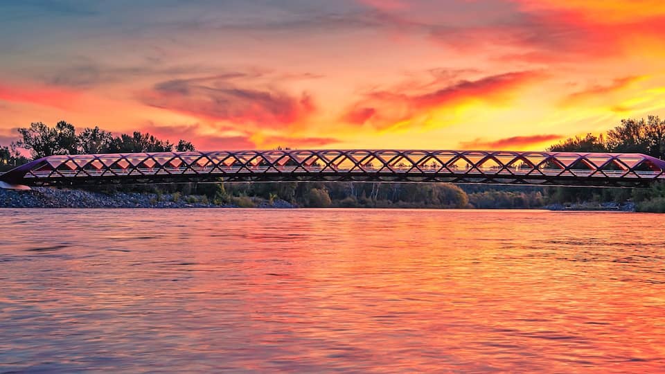 A bridge over a river at sunset with a colorful sky.